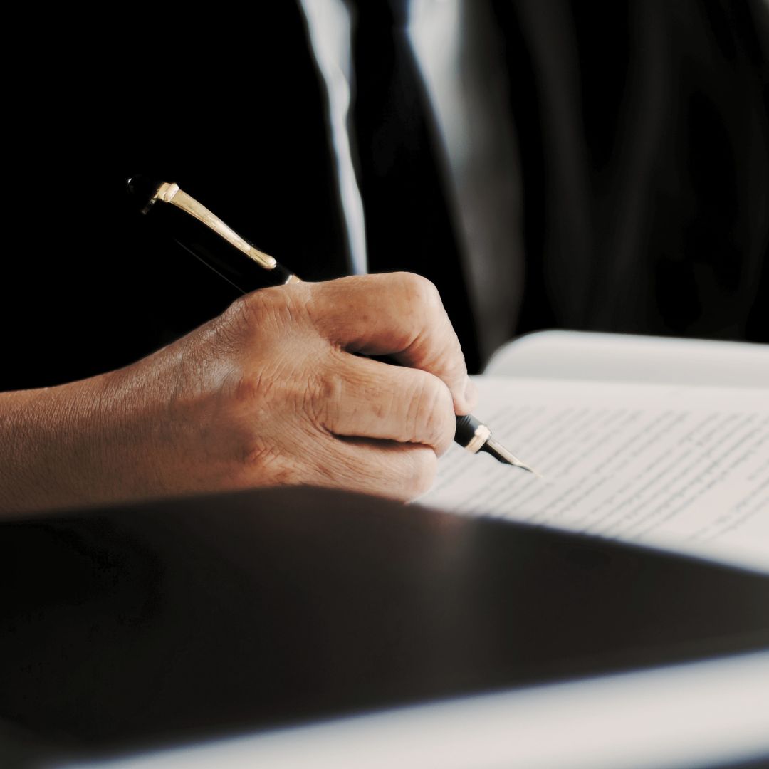 Senior hand signing a financial document with a fountain pen, illustrating the gravity of wealth management decisions and fiduciary mandates.